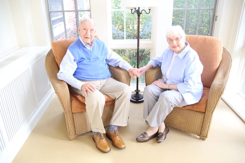 Senior couple sitting in armchairs holding hands. 