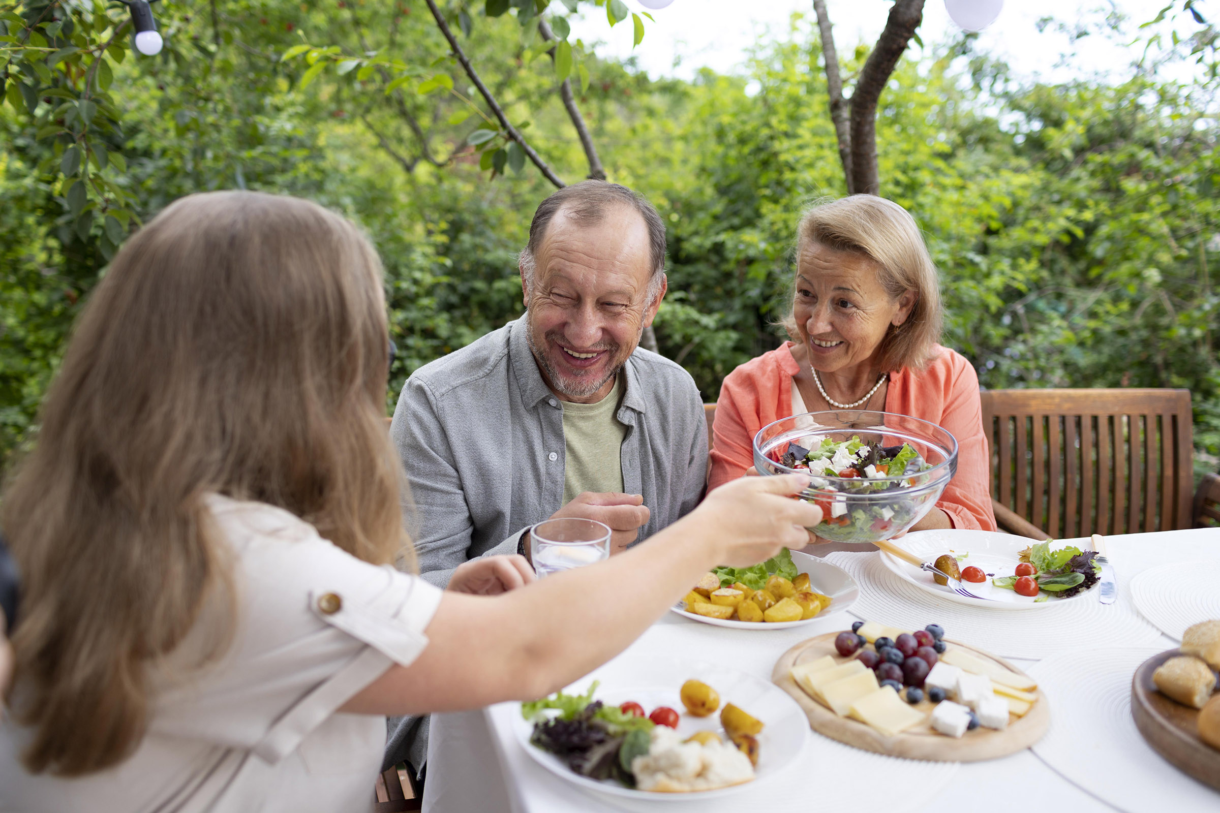 senior couple enjoy a meal outside with their daughter